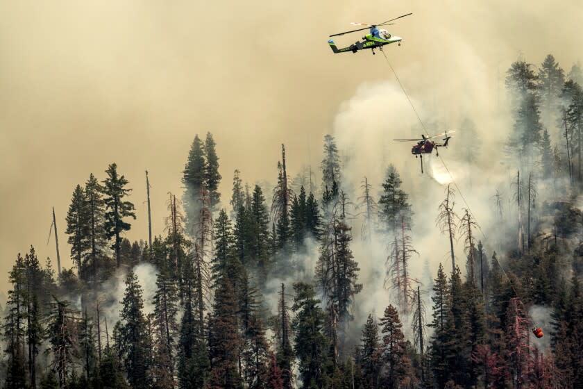 Seen from unincorporated Mariposa County, Calif., a helicopter drops water on the Washburn Fire burning in Yosemite National Park on Saturday, July 9, 2022. (AP Photo/Noah Berger)