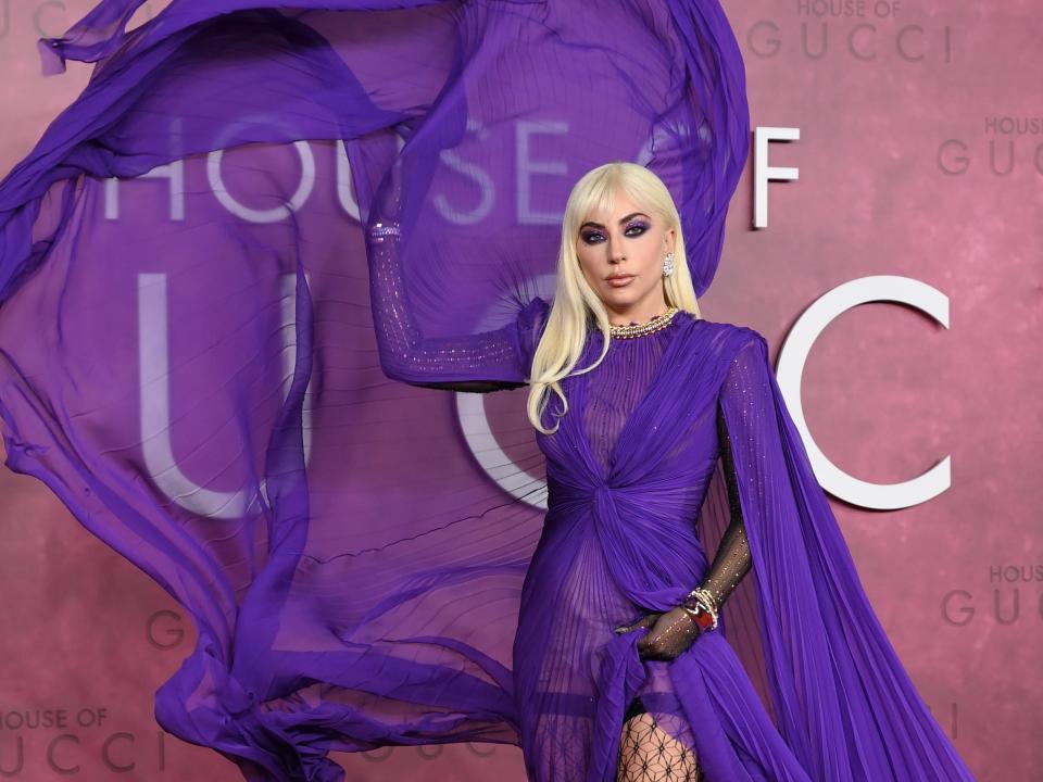 Lady Gaga on a red carpet in a bright purple dress and throwing the tulle cape in the air.