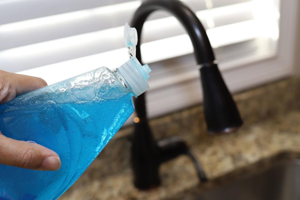 a woman holding a bottle of dish detergent in her hand