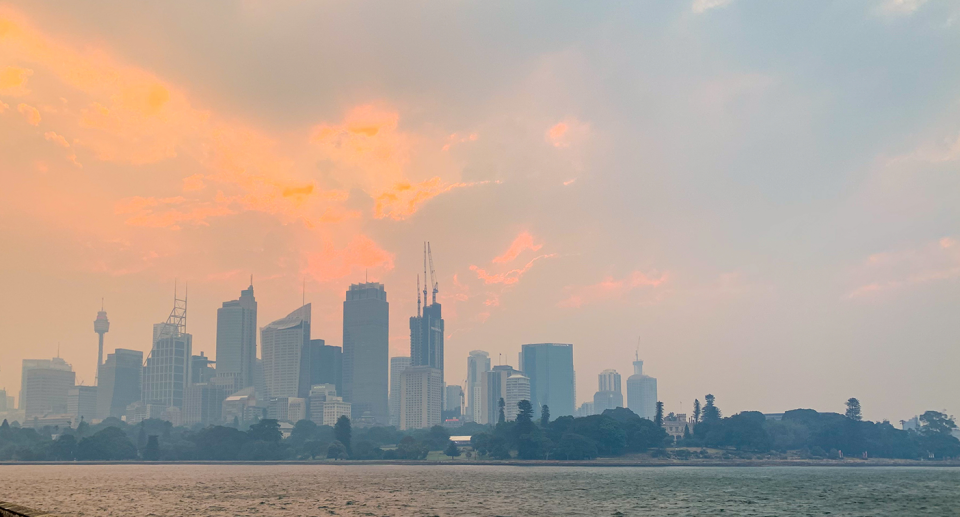 Sydney at a distance covered in smog with an orange sky.