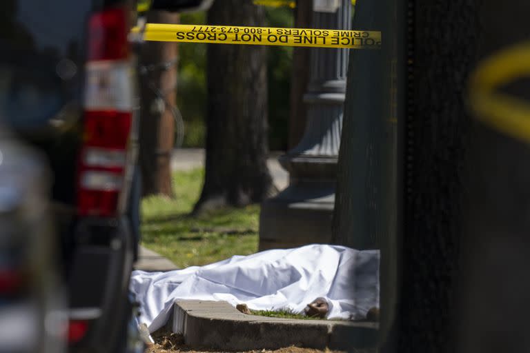 Una víctima bajo una sábana mientras agentes del Departamento de Policía Metropolitana investigan la escena de un tiroteo frente a la funeraria Stewart, el martes 11 de abril de 2023, en Washington D.C. (AP Foto/Alex Brandon)