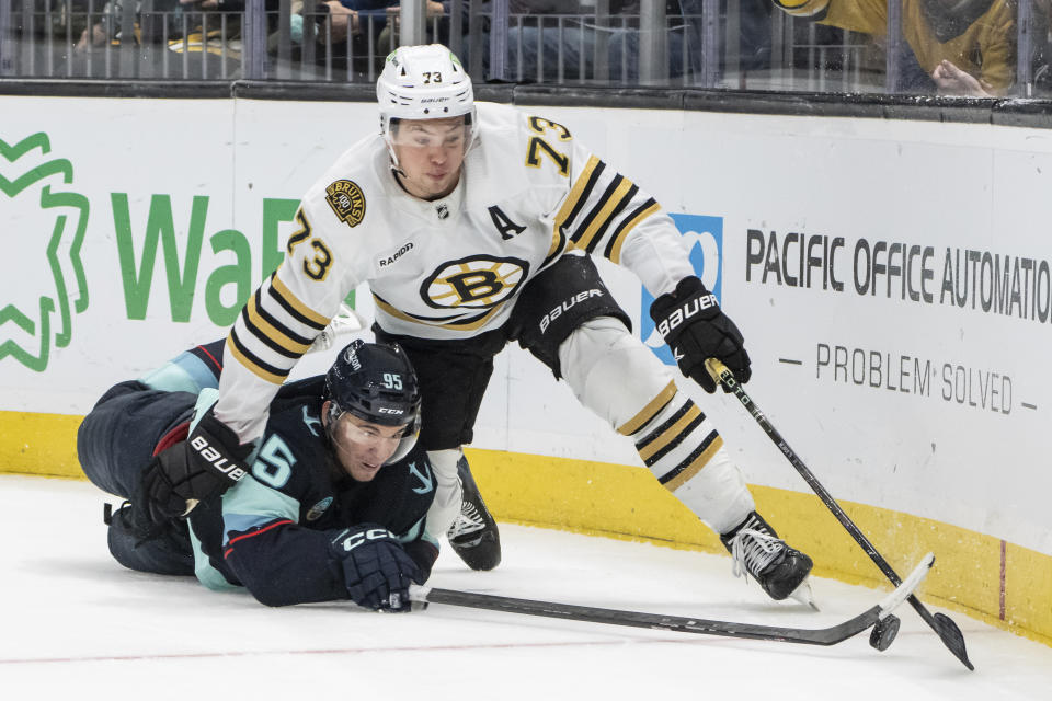 Boston Bruins defenseman Charlie McAvoy, right, and Seattle Kraken forward Andre Burakovsky battle for the puck during overtime of an NHL hockey game, Monday, Feb. 26, 2024, in Seattle. The Kraken won 4-3 in a shootout. (AP Photo/Stephen Brashear)