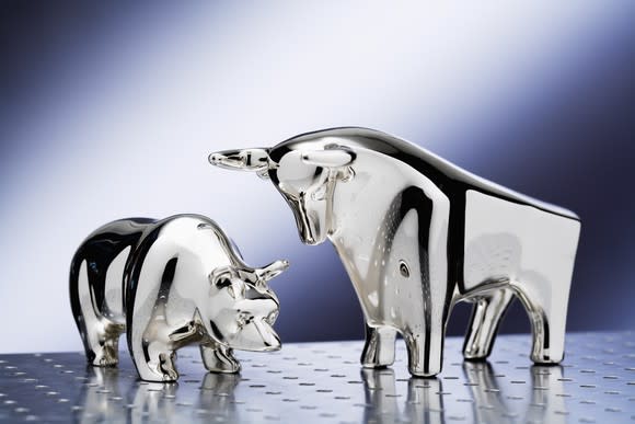 A glass bull and bear standing side by side on a steel surface.