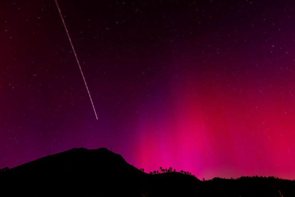 The blinking lights of a plane streak through the aurora borealis, also known as the Northern Lights, which is visible over Lake Berryessa, California.