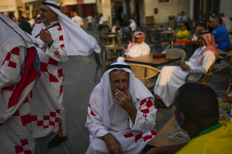 A Croatian supporter smokes as talks with a Brazilian fan, bottom right, one day ahead of the World Cup kick off, in downtown Doha, Qatar, Saturday, Nov. 19, 2022. (AP Photo/Francisco Seco)