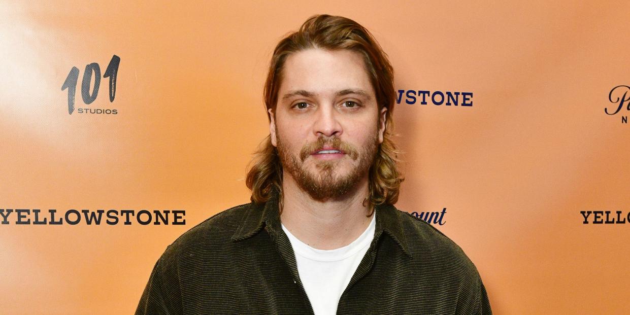 luke grimes wears his hair down to his shoulders and sports a corduroy shirt and white t shirt