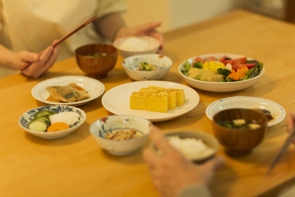 Various traditional Japanese dishes including tofu, vegetables, and rice on a wooden table with chopsticks in hand