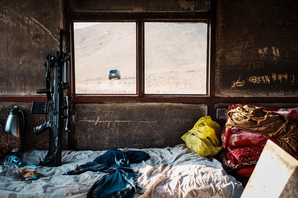 An assault weapon is propped up next to a window on a messy bed