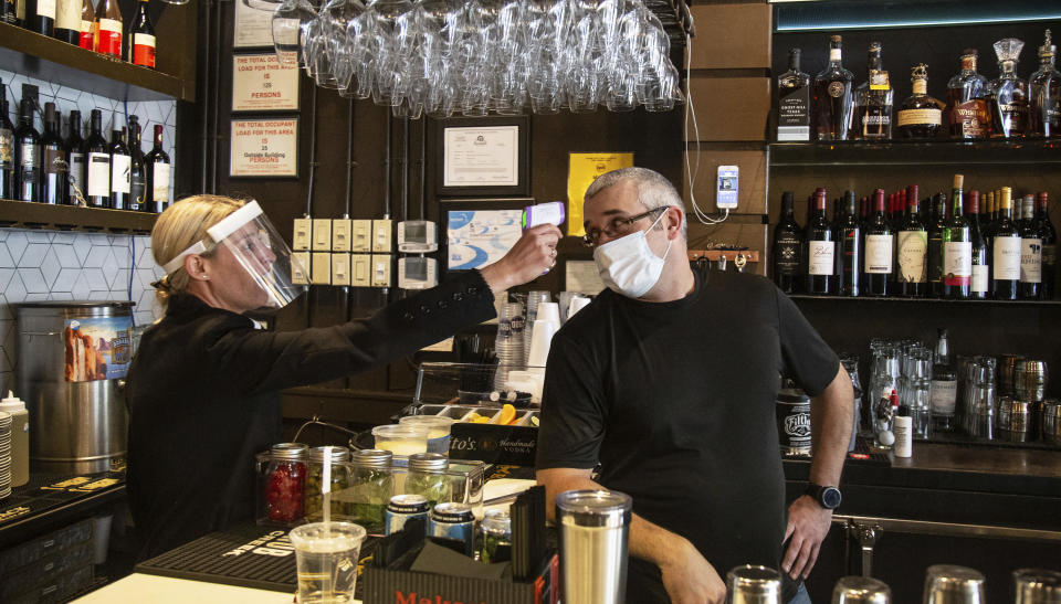 1920 Tavern Owner Jenna Aronowitz takes the temperature of bartender Shane Goode before the Roswell restaurant opens for sit down meals in Brookhaven, Ga., Monday, April 27, 2020. (Steve Schaefer/Atlanta Journal-Constitution via AP)