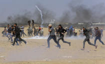 <p>Palestinian protesters run for cover from teargas fired by Israeli troops near the border fence, east of Khan Younis, in the Gaza Strip, Tuesday, May 15, 2018. Israel faced a growing backlash Tuesday and new charges of using excessive force, a day after Israeli troops firing from across a border fence killed 59 Palestinians and wounded more than 2,700 at a mass protest in Gaza. (Photo: Adel Hana/AP) </p>