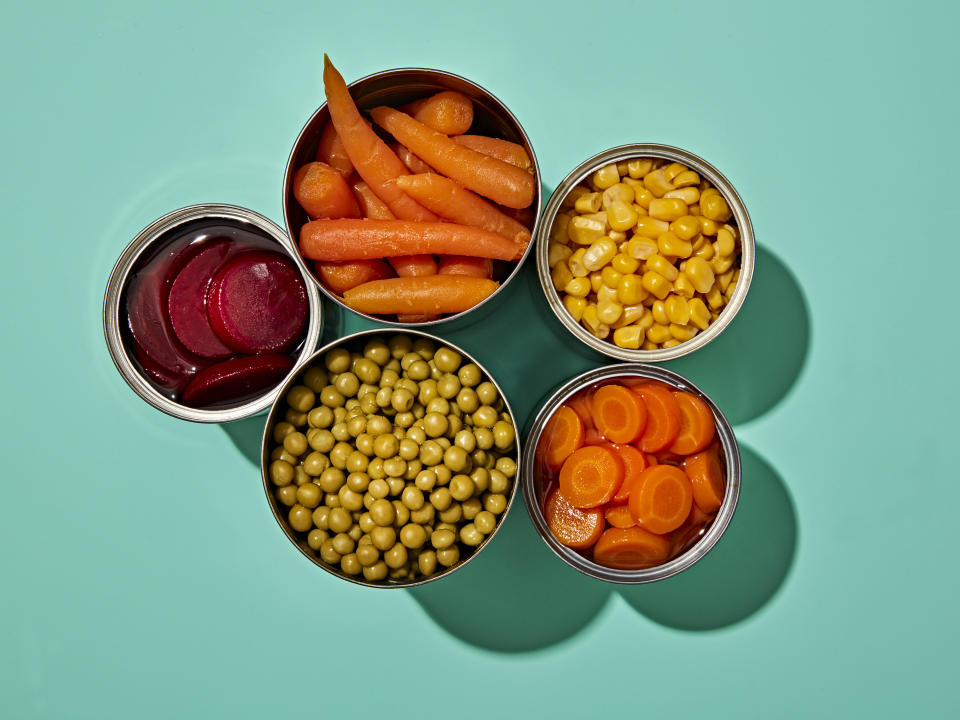 Canned carrots, corn peas and beets overhead view against a blue background