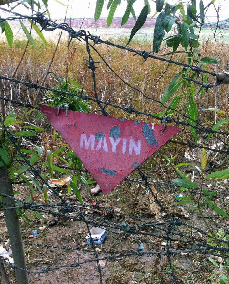 FILE - In this Nov. 19, 2012 file photo, a land mine sign at the Turkey-Syria border is seen from in Akinci village in Gaziantep province, Turkey. Starting in the 1950s, Turkish forces planted more than 600,000 U.S.-made "toe poppers" _ mines designed to maim, not kill _ and other land mines along much of its 900-kilometer (560-mile) border with Syria, which runs from the Mediterranean Sea to Iraq. The aim was to stop smugglers whose cheap black market goods undercut the Turkish economy and later to thwart Kurdish rebels from infiltrating Turkey's southeast. (AP Photo/Christopher Torchia, File)