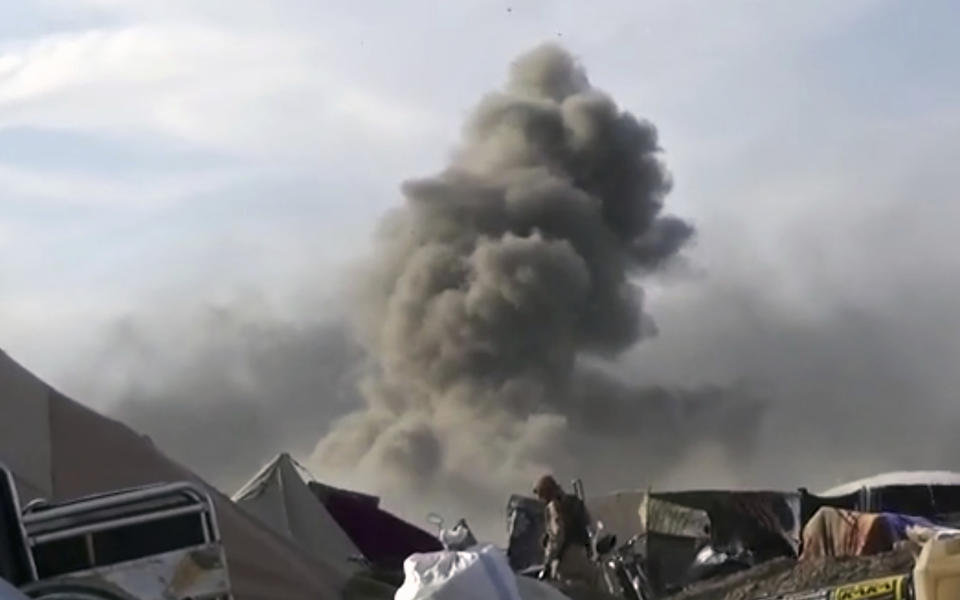 This frame grab from video posted online Monday, March 18, 2019, by the Aamaq News Agency, a media arm of the Islamic State group, shows smoke rising as an IS fighter walking inside Baghouz, the Islamic State group's last pocket of territory in Syria. U.S.-backed Syrian forces fighting the IS announced Tuesday they have taken control over an encampment in an eastern Syrian village where IS militants have been besieged for months, refusing to surrender. (Aamaq News Agency via AP)