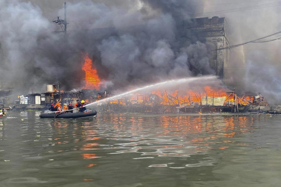 In this handout photo provided by the Philippine Coast Guard, members of the Philippine Coast Guard use a rubber boat as they train their hose on a cargo ship docked in Manila, Philippines on Saturday, June 12, 2021. The fire and a powerful blast ripped through a small cargo ship docked to refuel in the Philippine capital of Manila on Saturday, injuring at least six people and igniting a blaze in a nearby riverside slum that gutted dozens of shanties, officials said. (Philippine Coast Guard via AP)