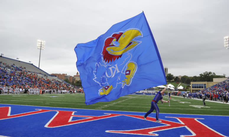 Kansas cheerleader runs with a Jayhawk flag during football game.