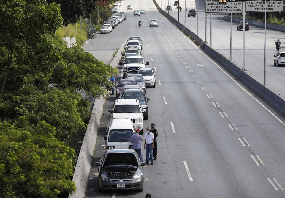 Men stand alongside vehicles lined up to enter a gas station during a nation-side fuel crunch, in Caracas, Venezuela, Wednesday, Sept 30, 2020. (AP Photo/Ariana Cubillos)