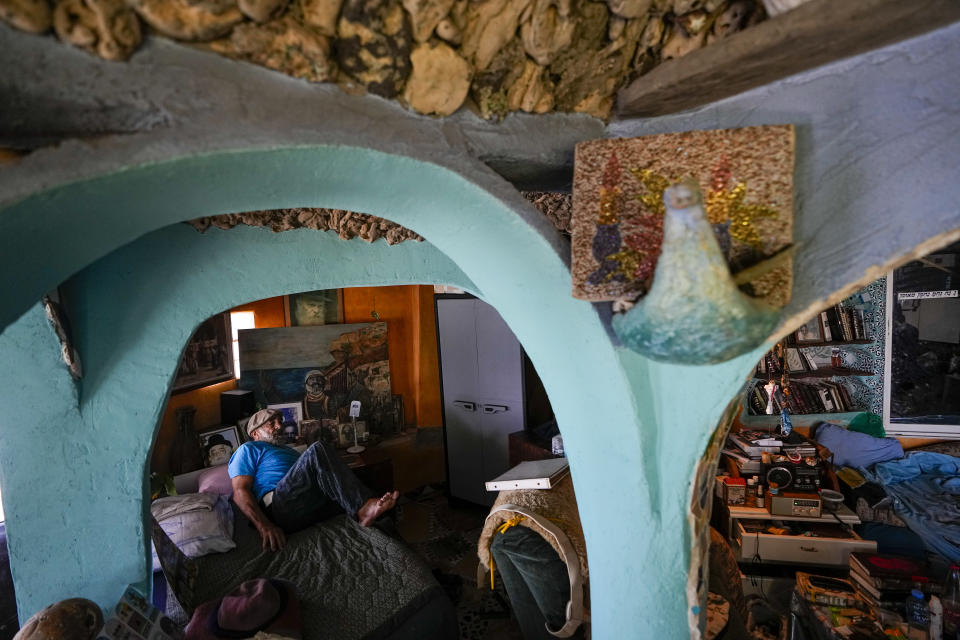 Nissim Kahlon gets up from his bed in his home chiseled out of the sandstone cliffs overlooking the Mediterranean sea in Herzliya, Israel, Wednesday, June 28, 2023. Over half a century, Kahlon has transformed a tiny cave on a Mediterranean beach into an elaborate underground labyrinth filled with chiseled tunnels, detailed mosaic floors and a network of staircases and mysterious chambers. Fifty years after Kahlon moved into the home, Israel's Environmental Protection Agency has served him an eviction notice, claiming the structure threatens Israel's coastline. (AP Photo/Ariel Schalit)