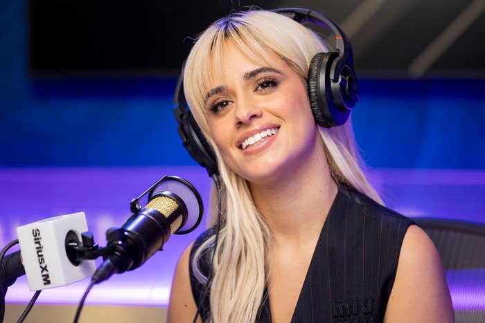 Camila Cabello smiles while wearing headphones and sitting at a SiriusXM radio station microphone