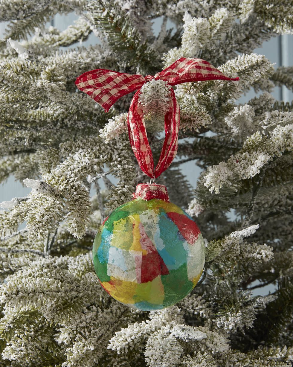 decoupaged tissue paper ornament in green, white, yellow and red, hanging on a flocked tree