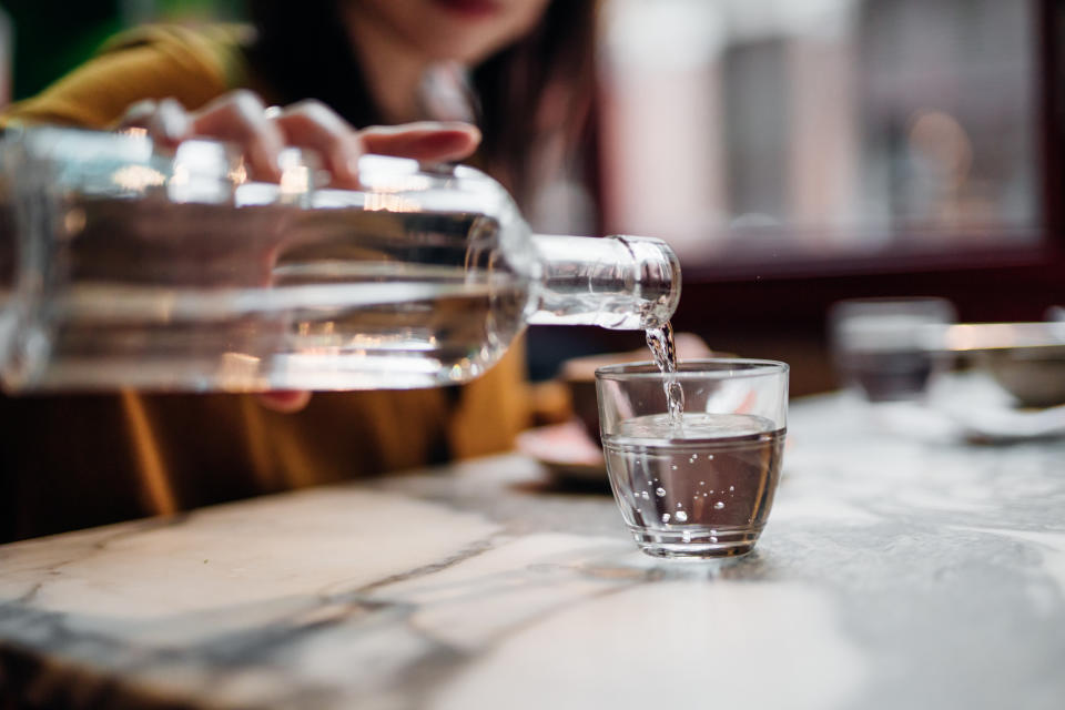 Close up einer Flasche Wasser, die von einer Frau ins Glas gegossen wird