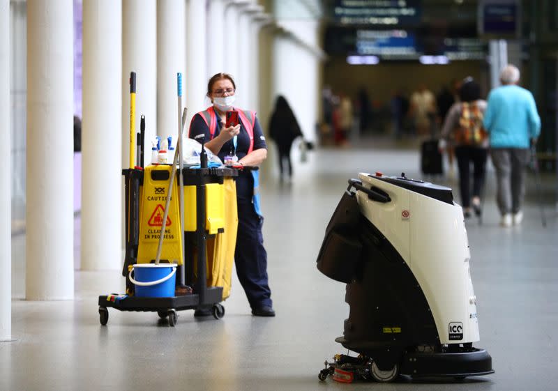 A cleaner photographs an Ultrasonic Disinfection Atomiser cleaning robot, known as an Eco Bot 50 as it cleans St Pancras International station in London