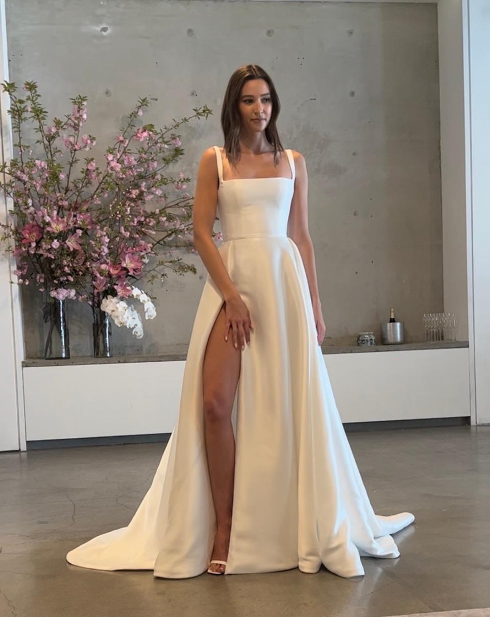 A woman stands in a wedding dress with a high slit.