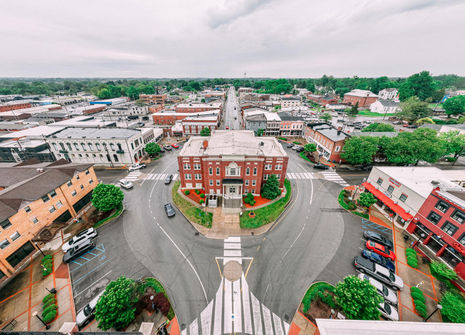 Aerial view of a town with a roundabout, buildings line the streets, and a cloudy sky above