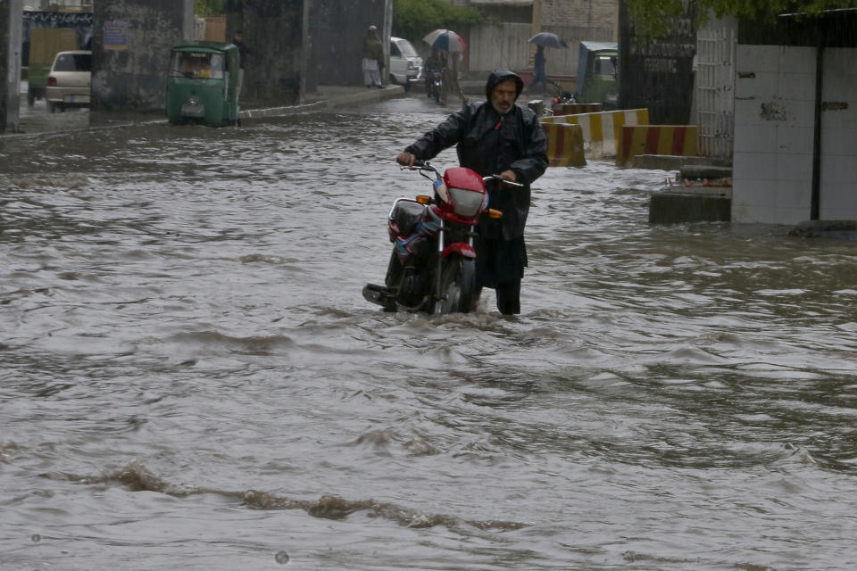 A Pakistani with his bike wades through a flooded road caused by heavy rain in Peshawar, Pakistan, Monday, April 15, 2024. Lightening and heavy rains killed dozens of people, mostly farmers, across Pakistan in the past three days, officials said Monday, as authorities declared a state of emergency in the country's southwest following an overnight rainfall to avoid any further casualties and damages. (AP Photo/Muhammad Sajjad)