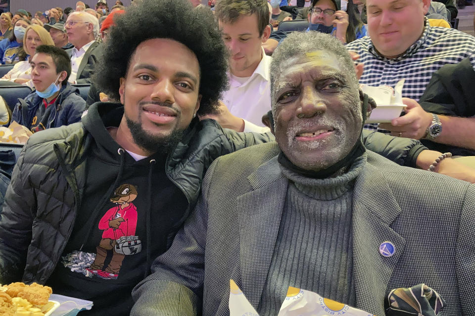 Golden State Warriors Hall of Famer Al Attles, right, sits with his grandson and Lincoln basketball player Isaiah Attles, at an NBA basketball game between the Warriors and the Los Angeles Clippers, Thursday, Oct. 21, 2021, in San Francisco. Hall of Famer Gary Payton is the new men's basketball coach at Lincoln University, determined to make a lasting mark in his hometown of Oakland, Calif. (AP Photo/Janie McCauley)