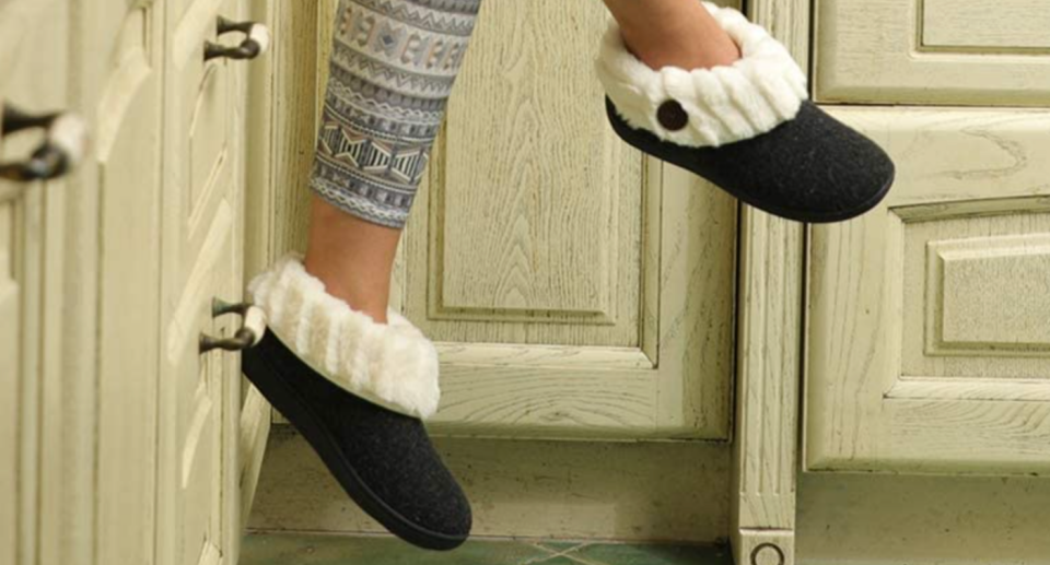 woman feet dangling wear black slippers with white faux fur sitting on kitchen cabinet