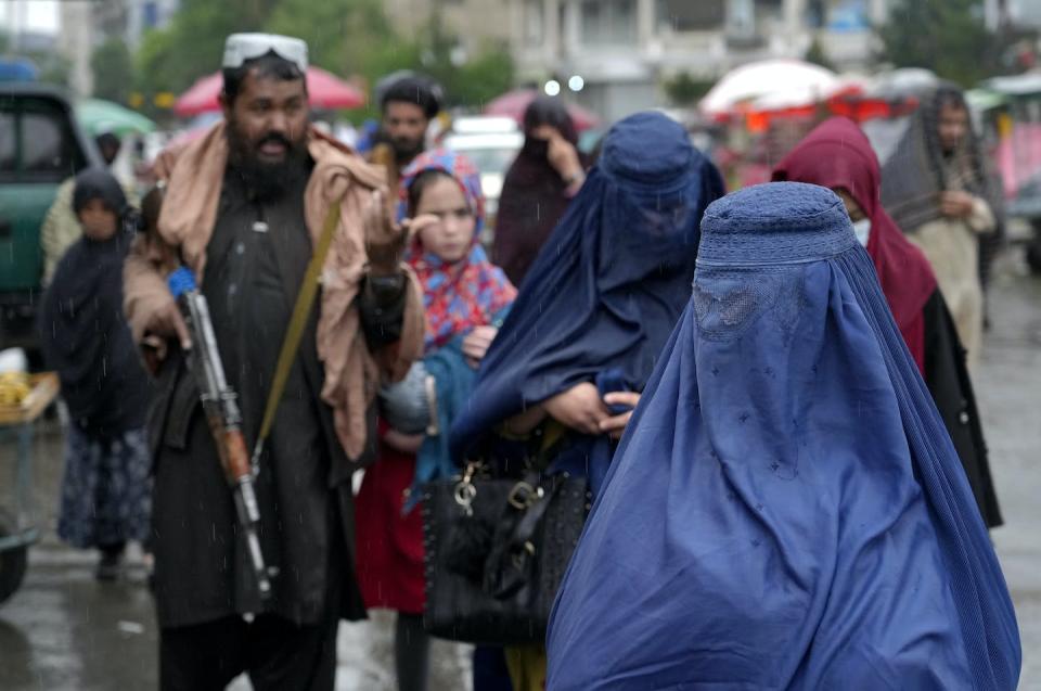 Mujeres afganas caminan por un mercado mientras un combatiente talibán monta guardia en el centro de Kabul, Afganistán, en mayo de 2022. AP Photo / Ebrahim Noroozi