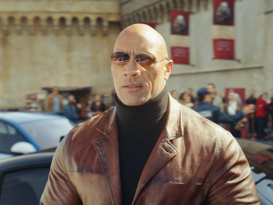 Dwayne Johnson in a leather jacket, black turtleneck, and glasses