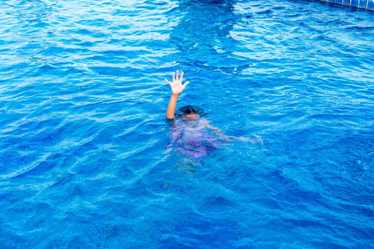 Female child has arm with hand raised for help as she is drowning in swimming pool