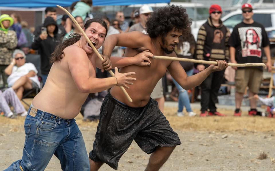 Young shirtless men play with sticks.