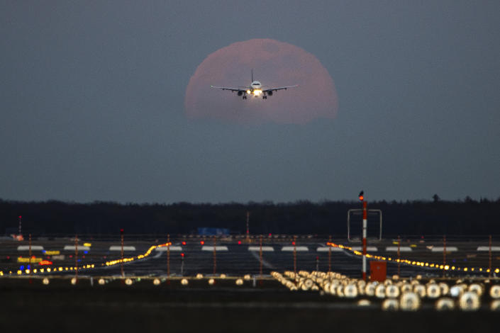 19 February 2019, Hessen, Frankfurt/Main: A passenger plane is landing at Frankfurt Airport, while the full moon is rising in the background.