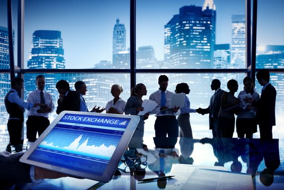 Group of people talking with a stock exchange display in the foreground.