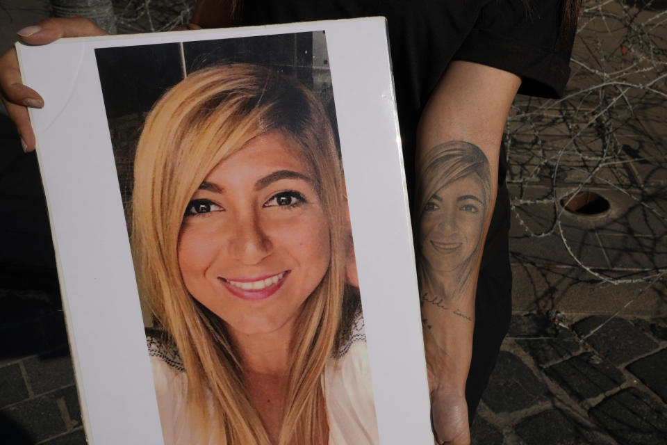 Mariana Fodoulian shows a tattoo and a portrait of her late sister Gaya Fodoulian during a protest near the parliament building to demand an expedited investigation, in Beirut, Lebanon, Sunday, July 4, 2021. Gaya Fodoulian died during the Aug. 4, 2020, Beirut port explosion. A year after the blast, families of the victims are consumed with winning justice for their loved ones and punishing Lebanon's political elite, blamed for causing the disaster through their corruption and neglect. Critics say the political leadership has succeeded so far in stonewalling the judicial investigation into the explosion. (AP Photo/Hassan Ammar)