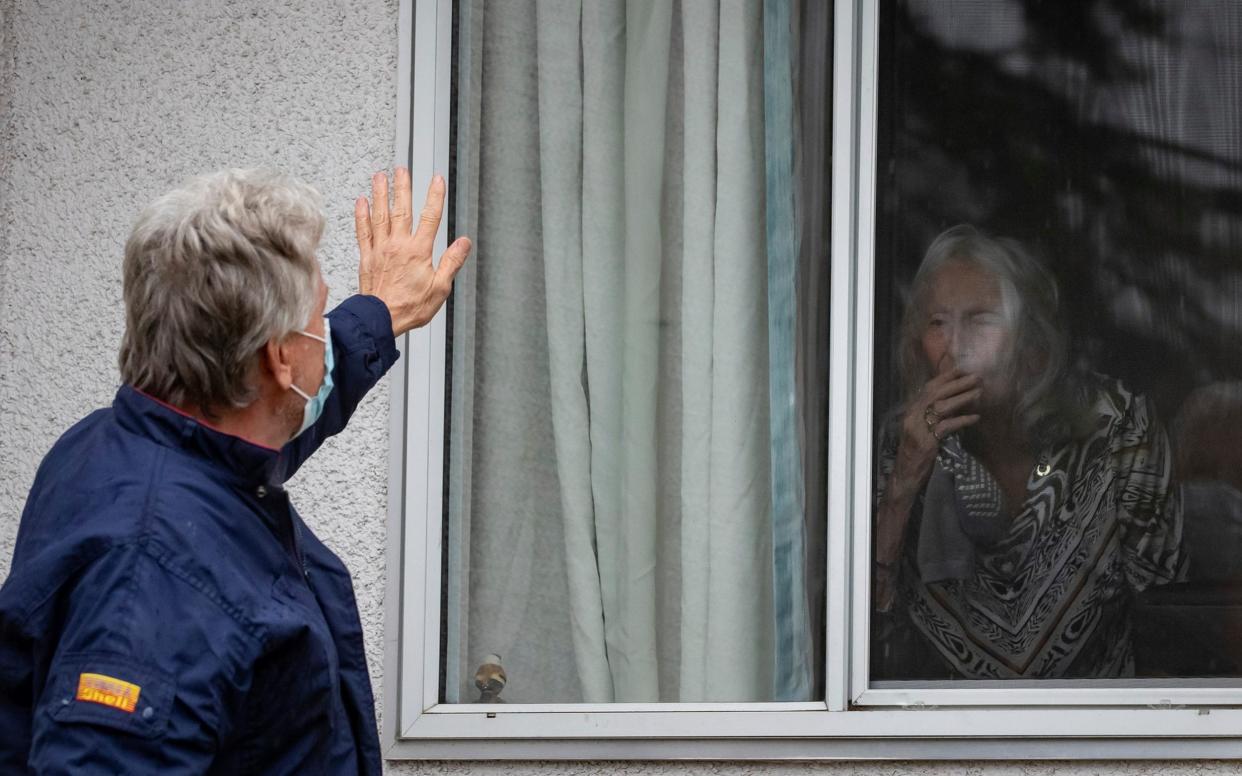 A man waves to his mother, who tested positive for Covid-19, through the window of her room in a care home - DARRYL DYCK /The Canadian Press 