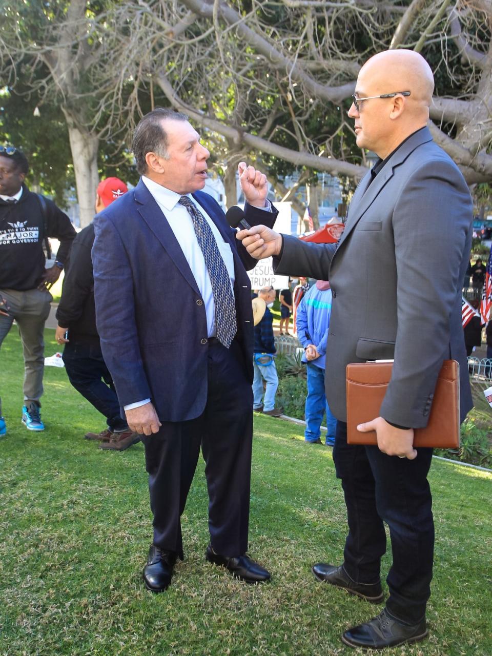 Two men stand on a grassy hill and speak to each other