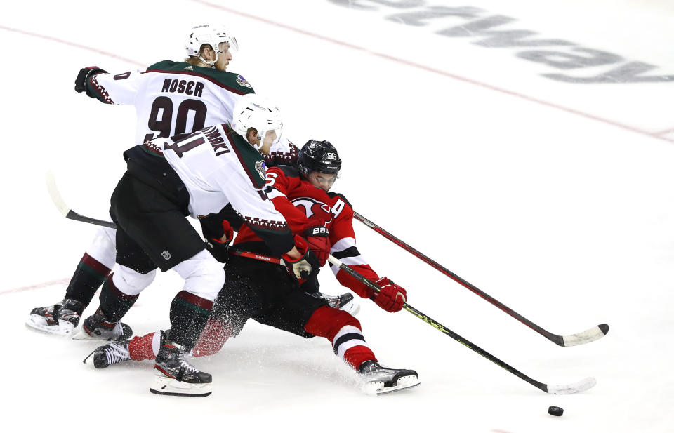 New Jersey Devils center Jack Hughes (86) plays the puck between Arizona Coyotes defensemen Juuso Valimaki (4) and J.J. Moser (90) during the third period of an NHL hockey game, Saturday, Nov. 12, 2022, in Newark, N.J. (AP Photo/Noah K. Murray)