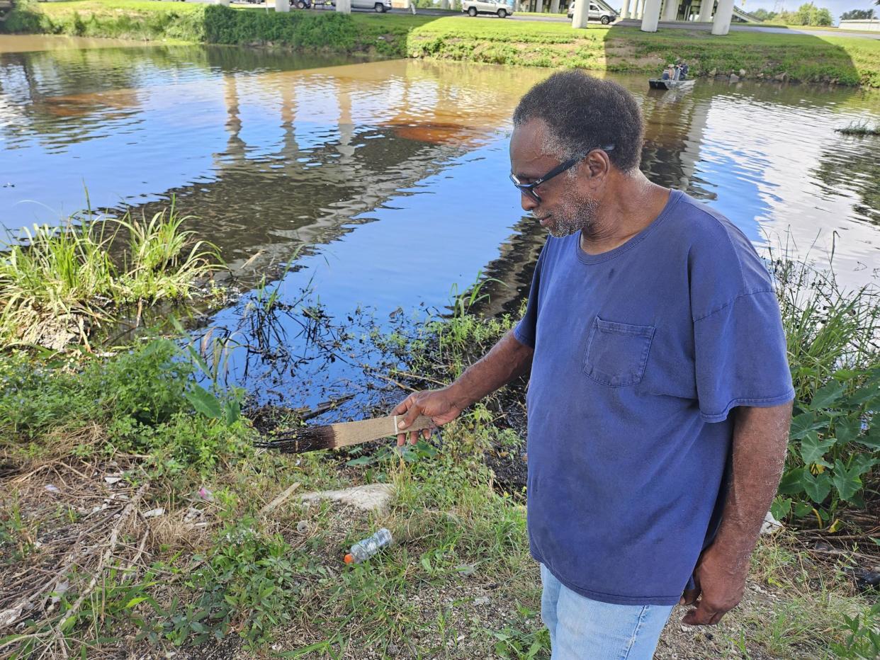 Bruce "Mike" Cleveland, holds a stick from Bayou Lafourche, covered in oil, Saturday, July 27. The oil escaped from a leak at a Crescent Midland facility between 4065 and 4101 LA 308.