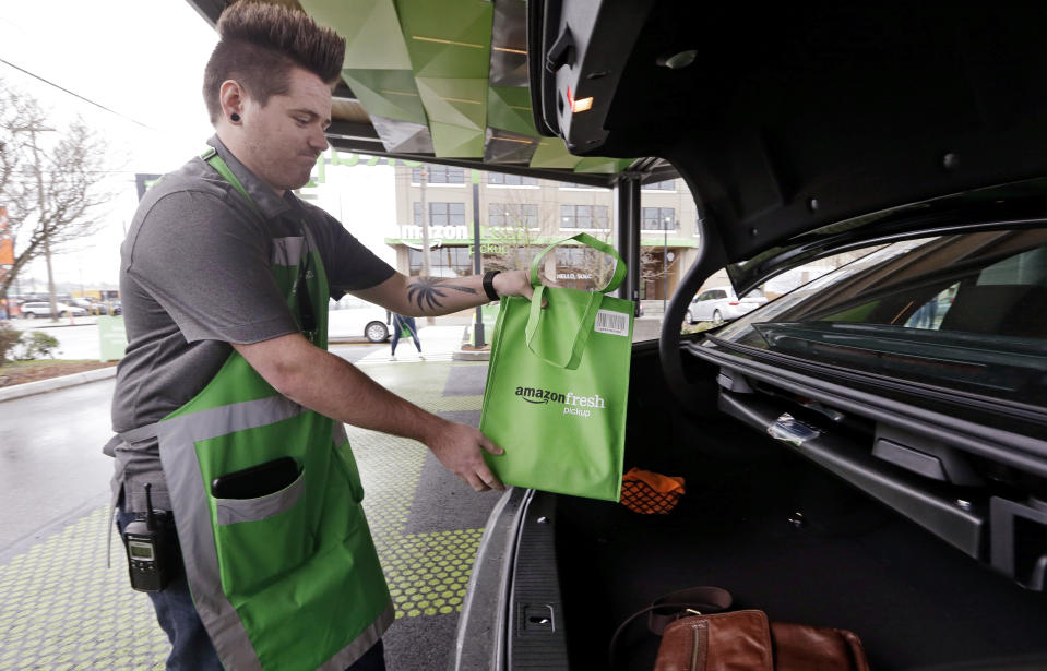 Un trabajador de Amazon coloca en el maletero del carro de un cliente un pedido en una estación de recogida de AmazonFresh en Seattle, EEUU. (AP Photo/Elaine Thompson)