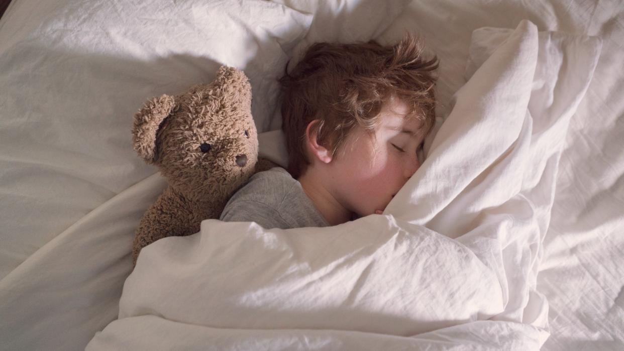  A boy sleeping in his bed with his teddy bear. 