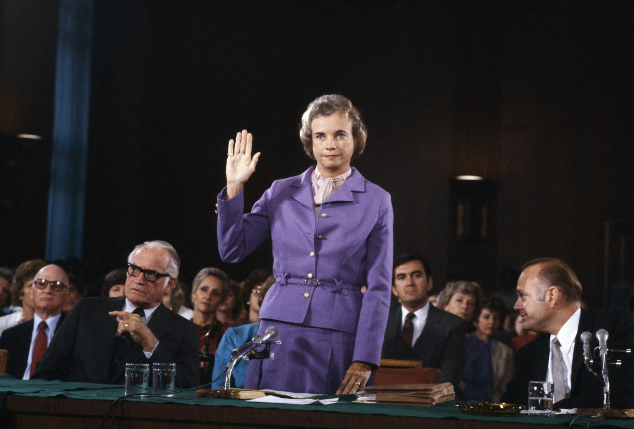 Sandra Day O’Connor, standing and wearing a purple suit, raises her right hand as she's sworn in before the Senate Judiciary Committee.
