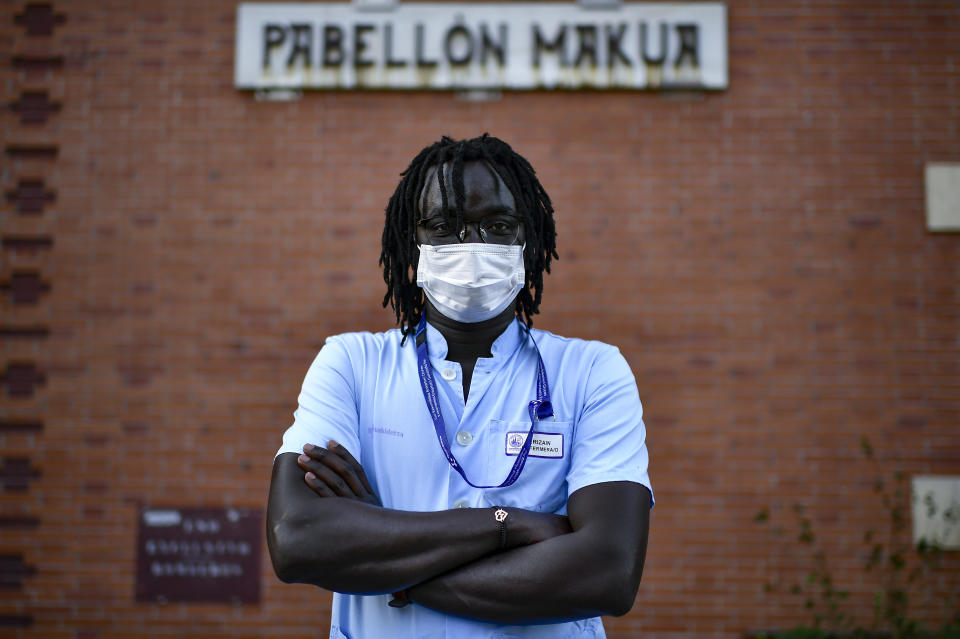 Mbaye Babacar Diouf, poses for a photo wearing his nurse's uniform, at Basurto hospital, in Bilbao, northern Spain, Wednesday, Nov. 18, 2020. Mbaye Babacar Diouf's life as a migrant in Europe took a turn for the better when he was adopted in Spain at the age of 28. That enabled him to pay his debts to human traffickers, study nursing and find a job at a Spanish hospital. Now he's giving back to the community. In a Bilbao hospital he cares for COVID-19 patients. (AP Photo/Alvaro Barrientos)