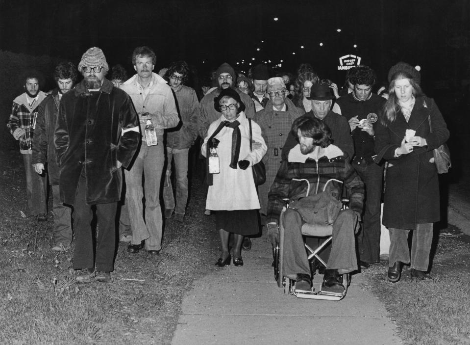 Professor Jerry Lewis (left, with beard), Elaine Holstein, mother of slain student Jeffrey Miller (center in white coat), and Dean Kahler (in wheelchair) participate May 3, 1976, in the annual candlelight vigil march to commemorate the shootings on the Kent State campus.