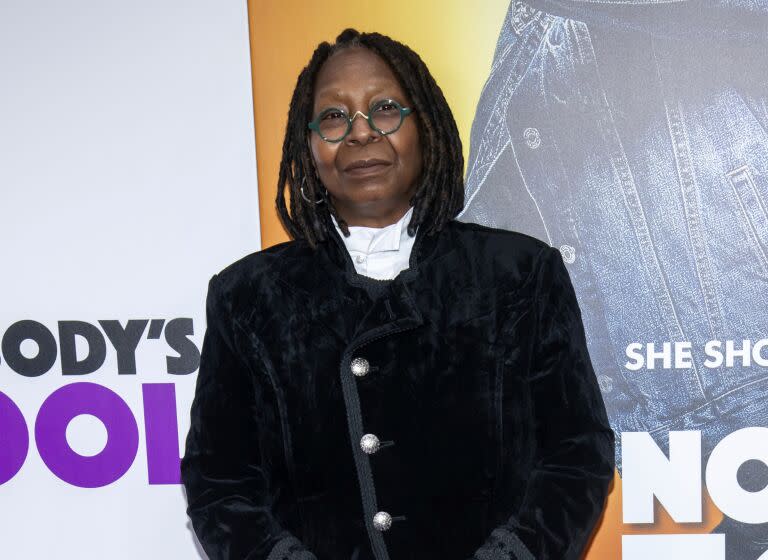Whoopi Goldberg in a black suit poses at a red carpet event