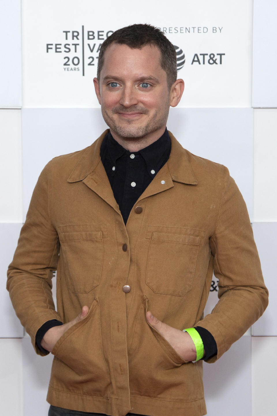 Smiling on the red carpet and wearing a casual shirt with hands in shirt pockets