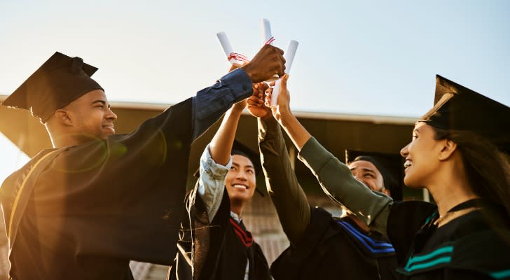 A group of college graduates celebrate by holding up their diplomas. 