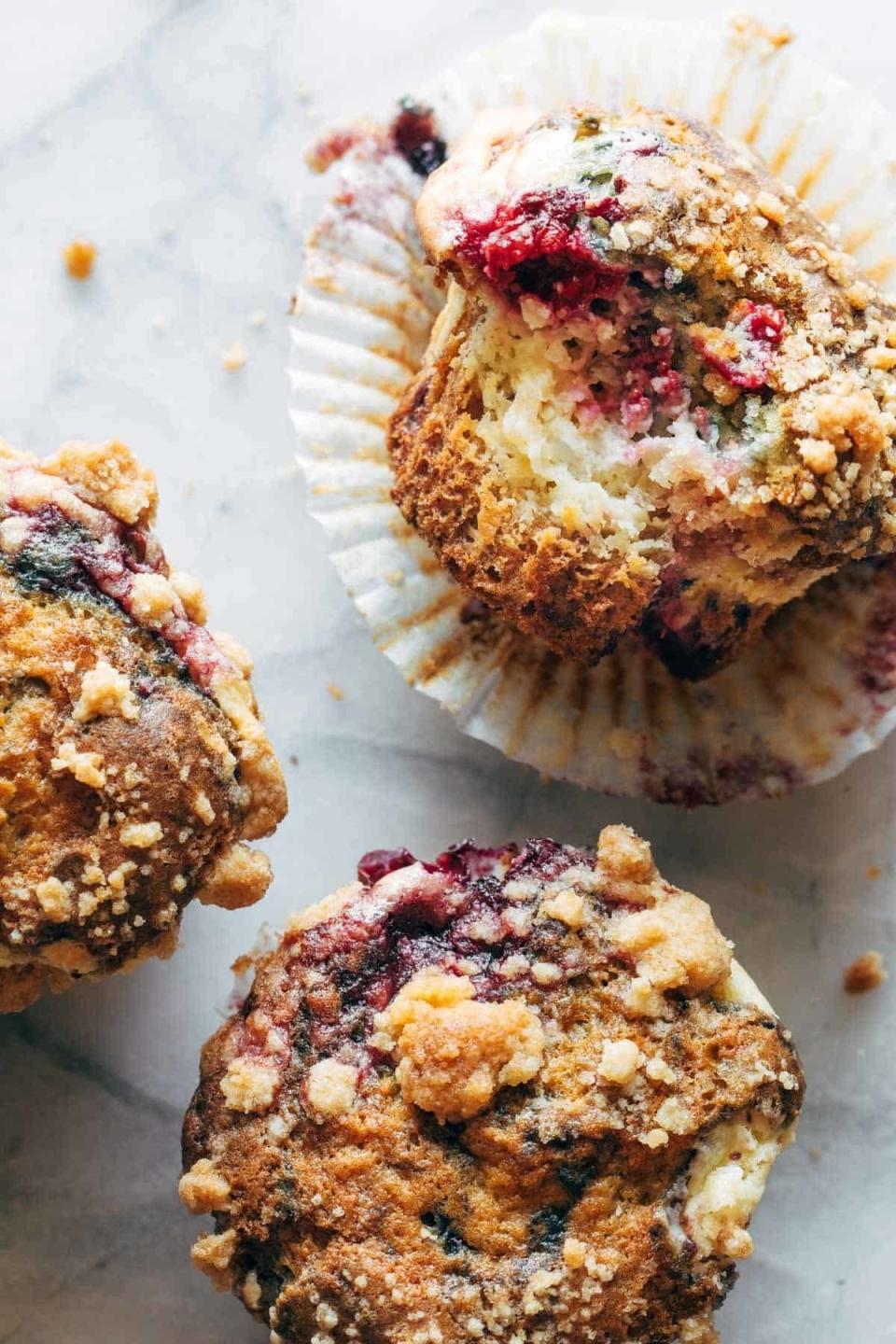 Close-up shot of three berry muffins with a crumbly topping. One muffin has a bite taken, revealing the berry filling inside